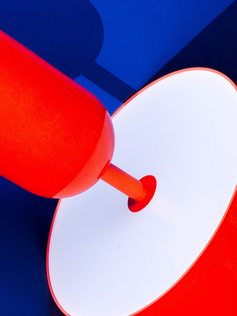 Abstracte productfoto van een Tom Dixon-lamp tegen een diepblauwe achtergrond. De feloranje en witte elementen van de lamp contrasteren sterk met de achtergrond, terwijl het schaduwspel een dynamisch effect toevoegt. Een modern en grafisch voorbeeld van productfotografie door Jasper Mulder