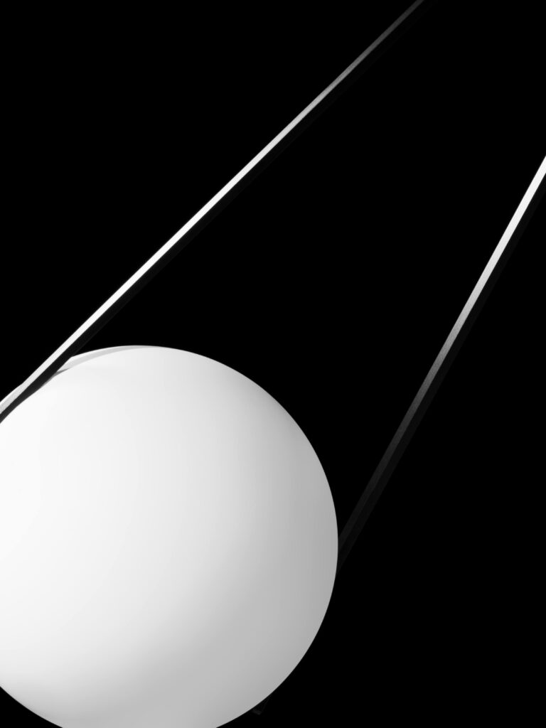 Minimalistische productfoto van een designlamp uit de collectie van Moooi. De witte bolvormige lamp hangt in een strakke, geometrische constructie tegen een diepzwarte achtergrond. Dit beeld speelt met licht en schaduw en benadrukt de moderne, abstracte esthetiek van de lamp. Een stijlvol voorbeeld van productfotografie, vastgelegd in Amsterdam door Jasper Mulder.