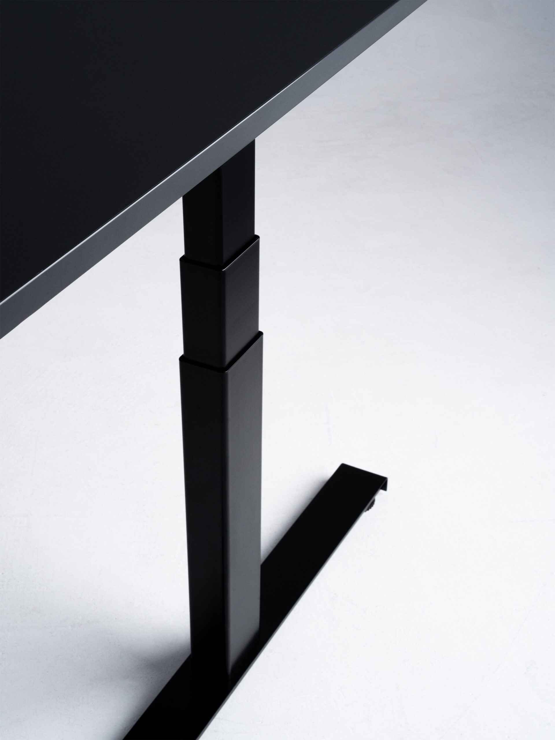 Minimalistische productfoto van een zwart zit-sta bureau met een stevig onderstel, vastgelegd tegen een lichte achtergrond. De scherpe lijnen en hoogwaardige afwerking benadrukken het strakke en functionele design. Professioneel gefotografeerd door Jasper Mulder in Amsterdam om de verfijnde details en duurzame constructie van het meubelstuk te tonen. Het product is van J. Kisch & Zonen, een gerenommeerd meubelmerk uit Amsterdam.
