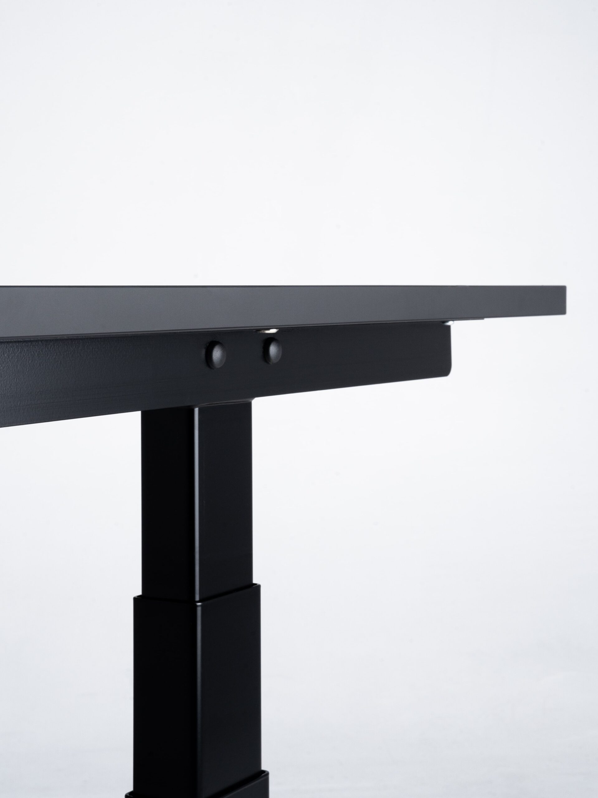 Minimalistische productfoto van een zwart zit-sta bureau, met een detailopname van het robuuste onderstel en de bevestigingselementen. De strakke lijnen en hoogwaardige afwerking benadrukken het moderne en functionele design. Professioneel gefotografeerd door Jasper Mulder, met oog voor detail en materiaalgebruik. Het product is van J. Kisch & Zonen, een gerenommeerd meubelmerk uit Amsterdam.