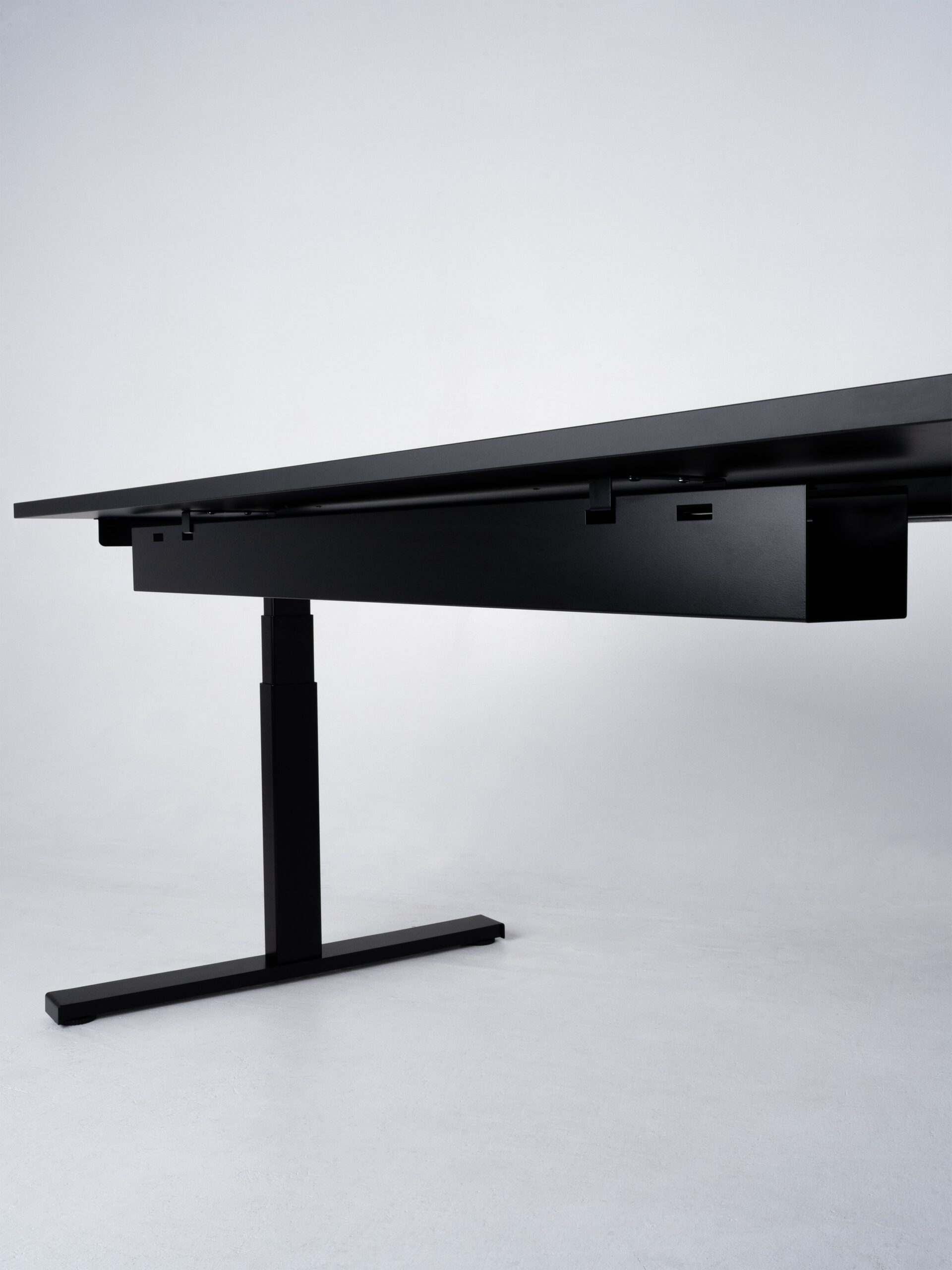 Minimalistische productfoto van een zwart zit-sta bureau, vastgelegd vanuit een laag perspectief om de onderzijde en het mechanisme te benadrukken. De strakke lijnen en industriële afwerking tonen de robuustheid en functionaliteit van het ontwerp. Professionele productfotografie door Jasper Mulder, met focus op de hoogwaardige afwerking en slimme technische details. Het product is van J. Kisch & Zonen, een gerenommeerd meubelmerk uit Amsterdam.