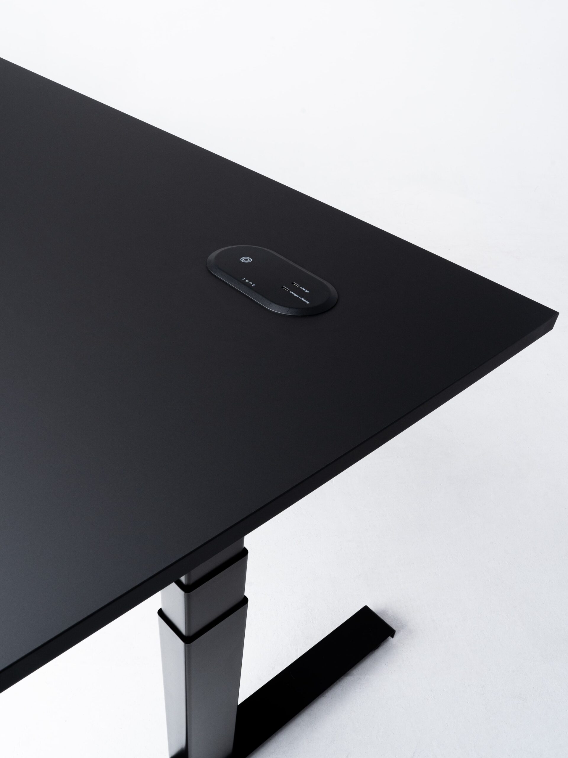 Minimalistische productfoto van een zwart zit-sta bureau met een geïntegreerd docking station, vastgelegd tegen een lichte achtergrond. De strakke lijnen en het subtiele contrast tussen materialen benadrukken het moderne en functionele ontwerp. Professionele productfotografie door Jasper Mulder, met focus op de hoogwaardige afwerking en slimme ergonomische details. Het product is van J. Kisch & Zonen, een gerenommeerd meubelmerk uit Amsterdam.