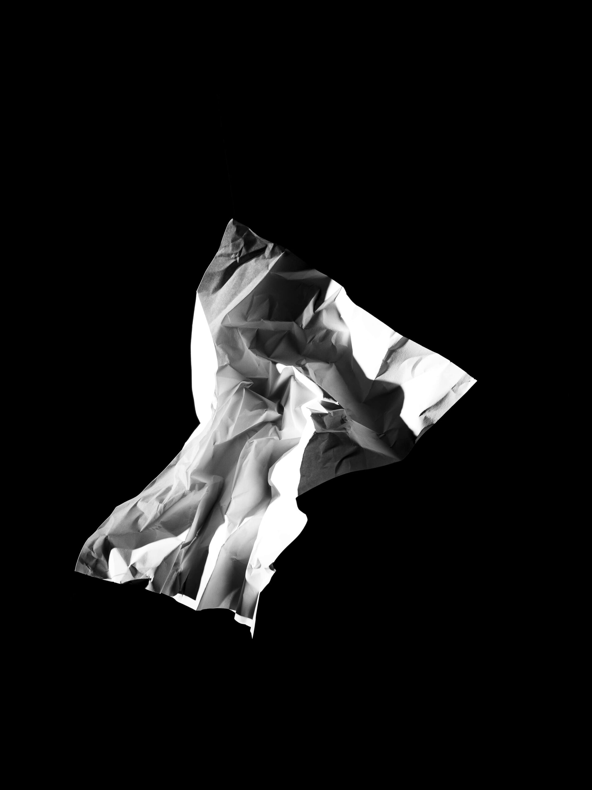 Minimalistische en abstracte compositie van een zwevende, gekreukte papieren vorm op een diepe zwarte achtergrond. Het scherpe lichtspel benadrukt textuur en vorm, en creëert een sculpturale aanwezigheid. Dit werk vangt de essentie van vergankelijkheid en materialiteit, en vormt een abstraherende basis van het werk van Jasper Mulder. Vastgelegd in Amsterdam.