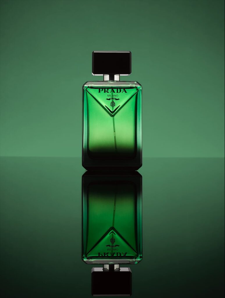 Studiofoto van een groene parfumfles van Prada Milano met zwarte dop, centraal geplaatst tegen een groene achtergrond. De fles heeft strakke, geometrische lijnen en wordt gespiegeld in een reflecterend oppervlak, waardoor een symmetrisch effect ontstaat. Beeld: www.jaspermulder.studio.